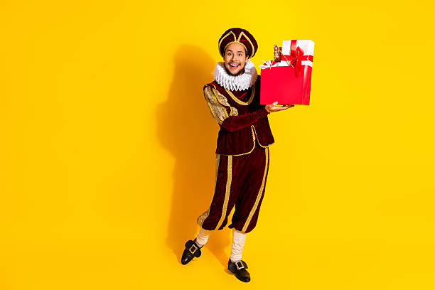 istock Man dressed as a medieval nobleman holding a red gift on a yellow background, evoking themes of history, celebration, and noble traditions. 2218202849