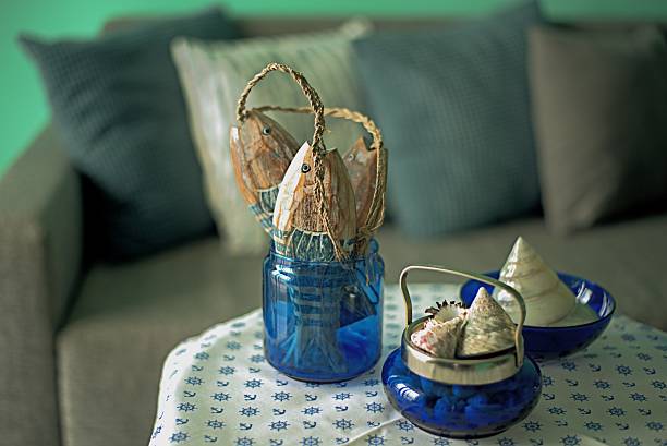 Marine style in the apartment interior - a sofa with pillows and a table with shells and fish figures. Blue room in a marine concept
