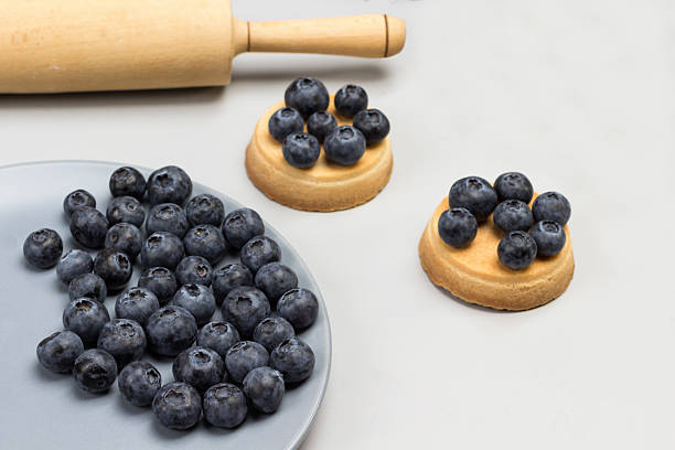 Blueberries on gray plate. Blueberry tartlets. Rolling pin and gray napkin. Gray background. Top view