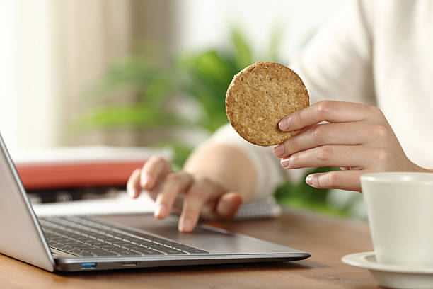 istock Student hand holding cookie using laptop on wooden table 2218205053