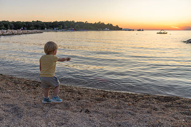 A European boy walks on the shore of a lake in the summer. A boy swims in the lake.