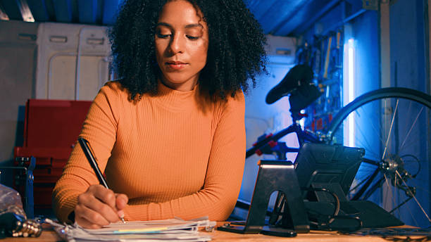 istock Focused Woman Writing in Garage Workspace With Bicycle and Tools in the Background 2218207508