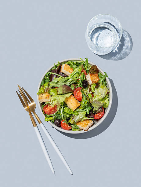 Vegetable salad with lettuce, tomatoes, croutons and olives in a bowl on a blue background