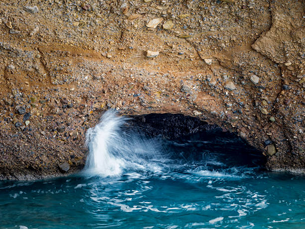 Turquoise water flows through a rock arch, contrasting beautifully with the earthy cliffside tones.