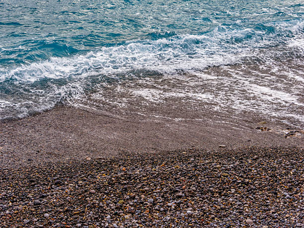 Water rushes over smooth pebbles along the coastline of Kalo Nero, showcasing Greece's serene natural beauty.