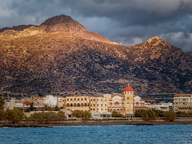 Golden mountains loom behind Ierapetra, while waves gently lap the shore, creating a serene seaside atmosphere.