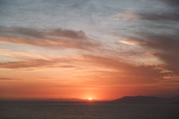 A serene sunset view over the ocean with hazy skies and soft clouds creating a dreamy atmosphere.