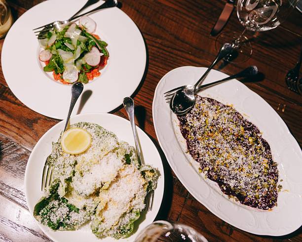 A top view of a dining table with three elegantly plated dishes, including a salad, a lemon-topped dish, and a sprinkled dessert.