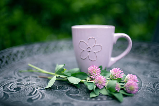A vibrant bouquet of wildflowers in shades of purple, yellow, red, and white is elegantly arranged in a small, weathered tin bucket on a rustic wooden table. The lush, blurred green background creates a serene outdoor setting, evoking the charm of a countryside garden. The soft bokeh effect enhances the natural beauty of the flowers, making this image ideal for themes related to nature, spring, gardening, and rustic decor.