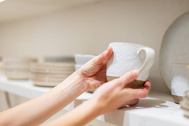 Hands gripping a ceramic mug while selecting kitchenware from a shelf in a vibrant home goods store, embodying a shopping experience