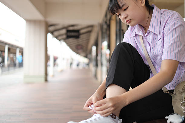 The East Asian woman is trying on her new shoes outside the shopping mall.
