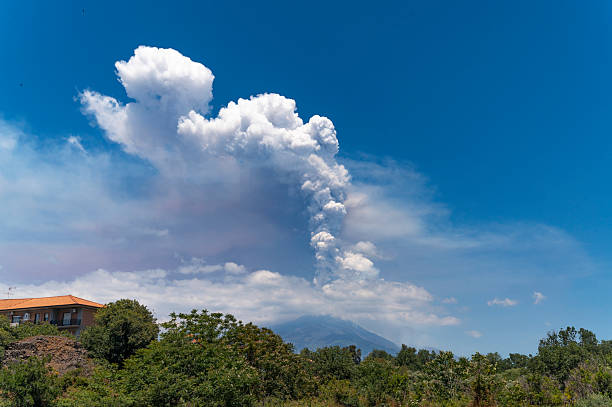 Mount Etna dominates the Sicilian skyline with a distinct volcanic form. Smoke rises gently from the summit above the valley below