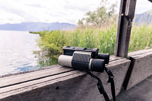 Binoculars resting on a wooden ledge with a panoramic lake view. Scenic mountain landscape in the background. Perfect for outdoor and adventure themes.