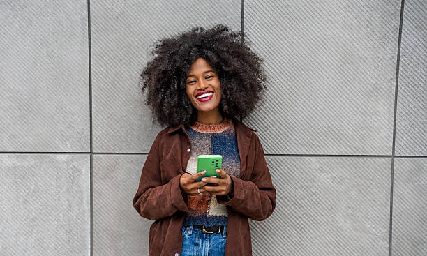 istock Young woman using mobile phone and smiling by a gray wall 2218238546