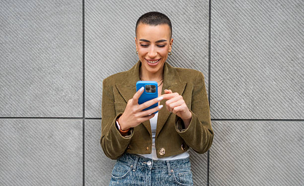 istock Young woman using mobile phone and smiling near gray wall 2218239519