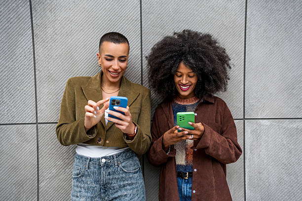 istock Two young women using smartphones and smiling by gray wall 2218239810