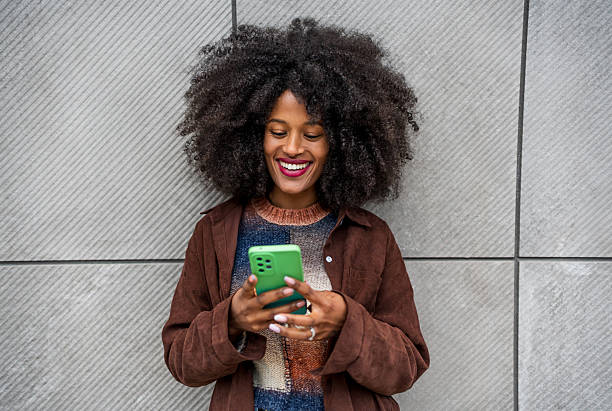 istock Young woman smiling and using mobile phone against gray wall 2218239941