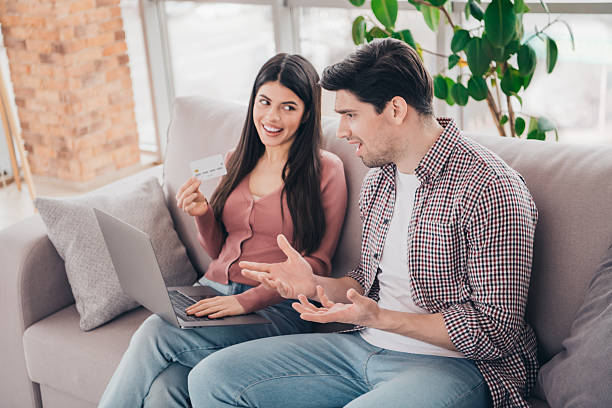 istock Young couple shopping online with a laptop, engaging in cheerful conversation while relaxing indoors on a comfy couch 2218241679