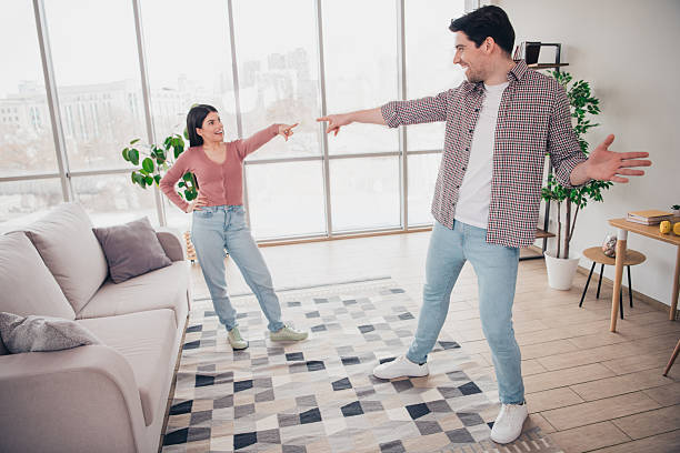 istock Young couple happily pointing at each other and laughing while spending relaxed moments together in a cozy apartment living room. 2218241720