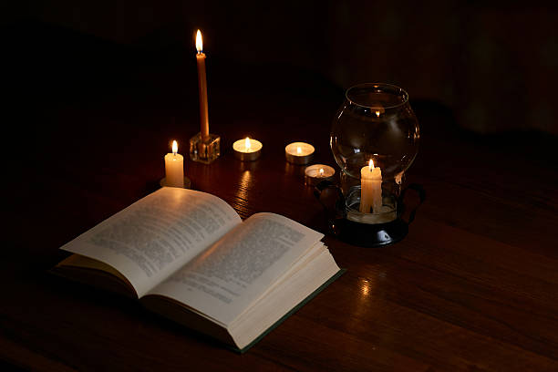 istock Reading a book by candlelight in a dark room. Blackout 2218246048