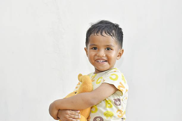 3 year old southeast asian child hugging doll smiling on white background