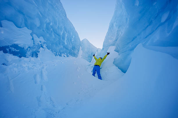 Standing in a snowy ice canyon, a man figure in a vibrant yellow coat joyfully lifts hands