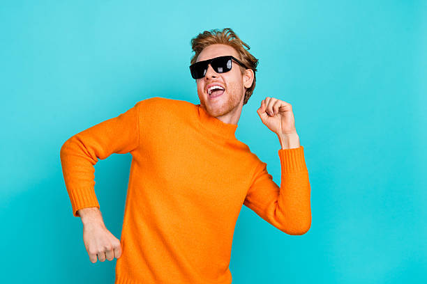 istock Photo of charming funky young man wear orange pullover dark spectacles dancing smiling isolated teal color background 2218259936