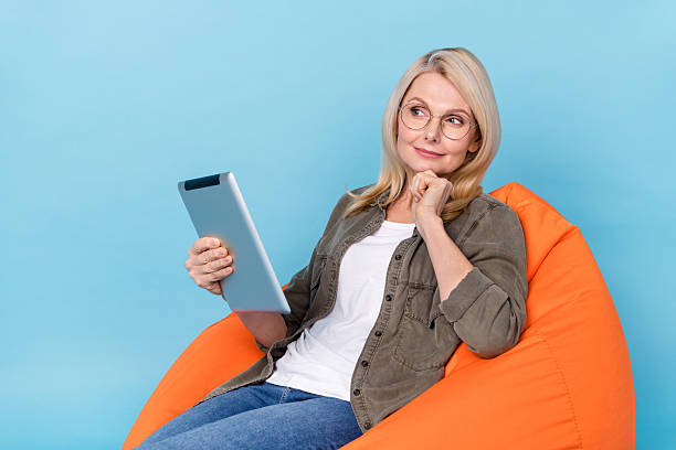 istock Photo of minded middle aged lady sit bag chair use tablet read e-reader deep think info isolated blue color background 2218262938