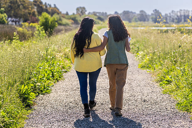 13 year old twin sisters walk together while hugging each other outdoors at dusk
