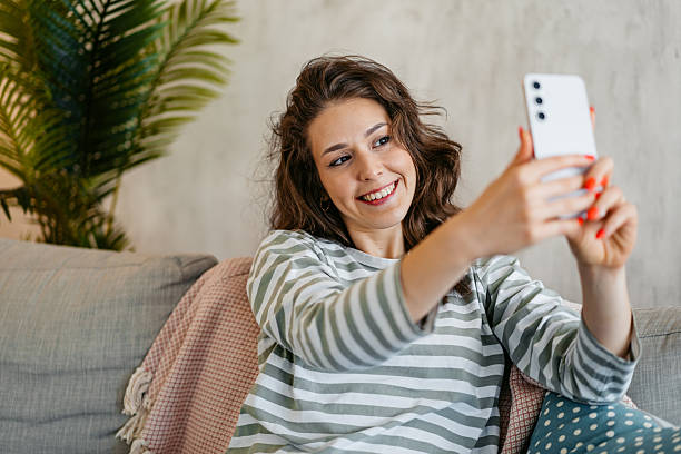 istock Young Woman Taking Selfies Using Phone While Sitting On The Sofa At Home 2218267357