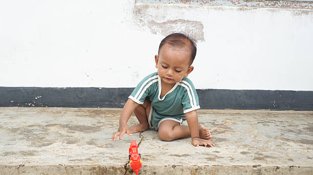 A small boy sitting and holding a toy motorcycle on a concrete surface, focused in a playful moment.