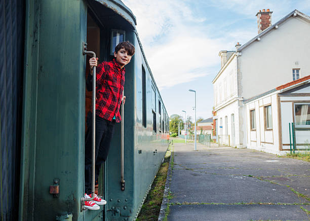 Teenager boy stands in the doorway of the green carriage, waiting for departure on a station, happy to travel by train during summer family vacations