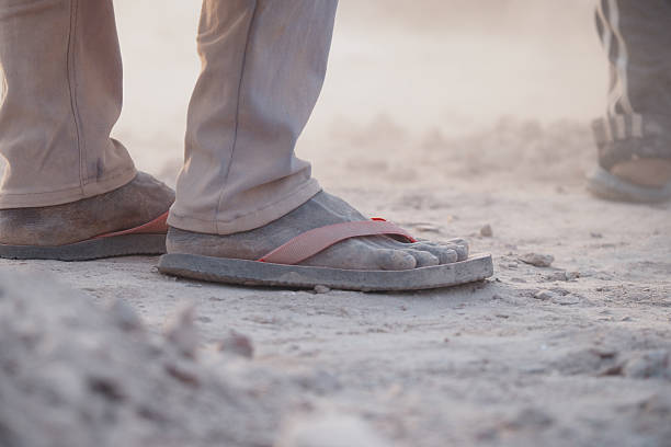 Dust covers worn sandals on a busy construction site in sunlight.