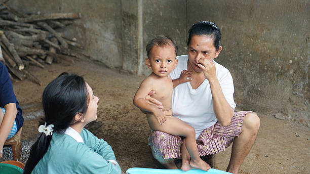 A toddler cries while being held by two adults for a bath, showing discomfort and resistance during hygiene care.