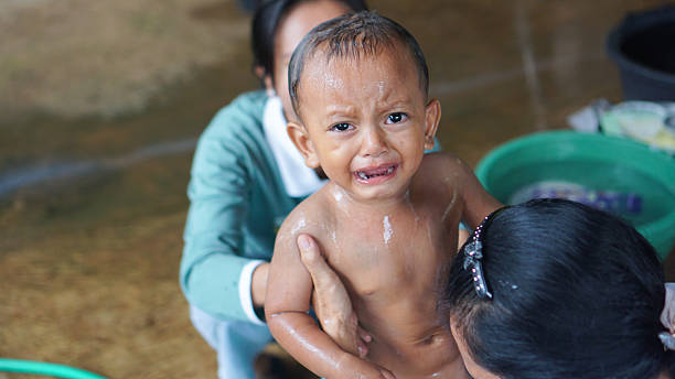 A young boy cries while being bathed at home by adults, showing a natural and emotional moment of parenting care.