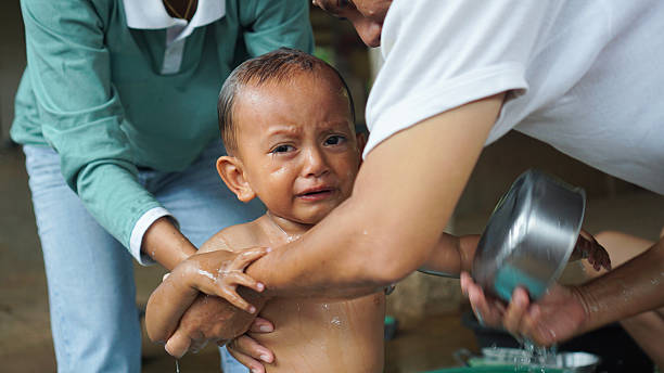 A young boy cries while being bathed at home by adults, showing a natural and emotional moment of parenting care.