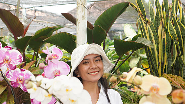 A cheerful woman in a white outfit and hat standing in a garden full of blooming orchid flowers.