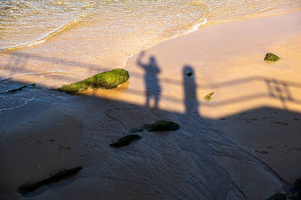 Long shadows of a couple cast on the sand at Isla Canela beach in Huelva, Spain, during the late sunset hours. This symbolic and serene scene captures the beauty of golden hour, ideal for concepts of love, connection, and peaceful moments.