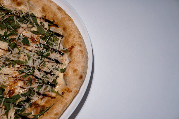 Delicious pizza with mozzarella, arugula, balsamic glaze served on a white plate, close-up shot, food photography.