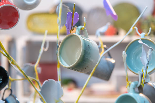 A vibrant display of ceramic cups in various colors hangs from a decorative branch at a local market. This setting showcases the craftsmanship and artistic flair of local artisans.