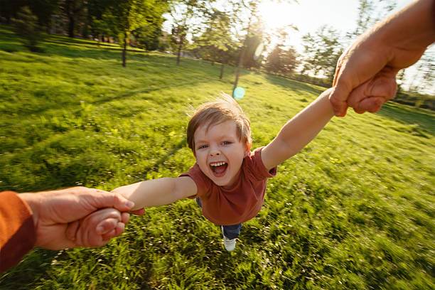 istock Father holding his son's hands, spinning him around in a circle at the park 2218285073