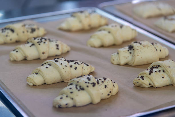 Freshly prepared croissant dough awaits baking on a tray lined with parchment paper. The pastries are topped with chocolate chips, showcasing a delightful treat for breakfast or dessert.