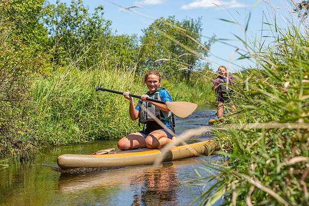Teenage girls (sisters) paddling upstream on their paddle boards on a summer day at the lake.