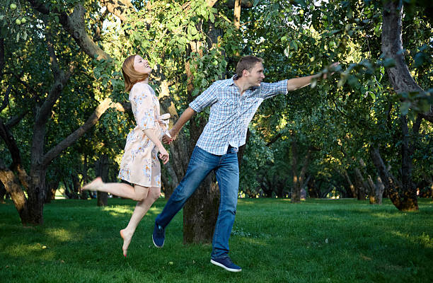 Beautiful young couple at a walk together in the park. They are jump holding hands. Shooting in the summer in the evening