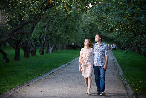 Beautiful young couple are walking together  in the park. They are looking up dreamily. Shooting in the summer in the evening