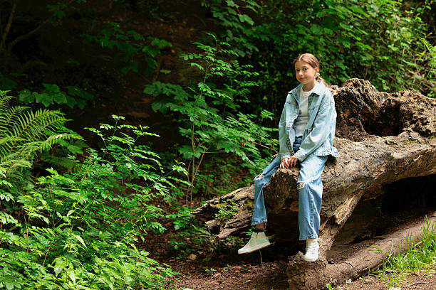 istock Young girl sitting on a fallen tree in woodland 2218295599