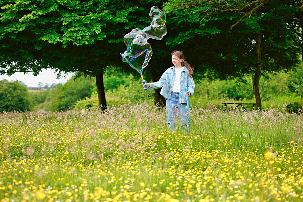 Pre-teen girl outdoors making bubbles in a meadow.