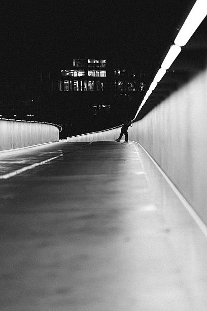istock Silhouetted Figure on Futuristic Pedestrian Bridge at Night 2218304355