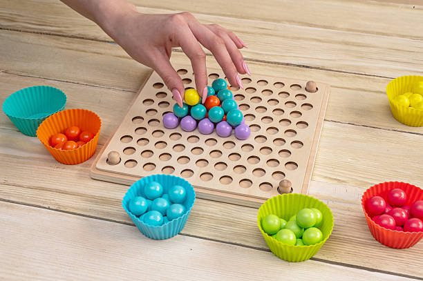 Educational game, wooden board for sorting according to the Montessori system. In her hands are wooden tweezers with a ball.