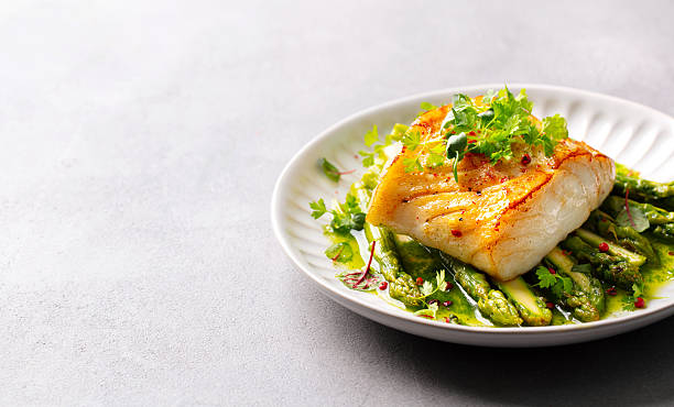 istock Roasted cod with asparagus and on plate. Grey background. Close up. Copy space. 2218308865